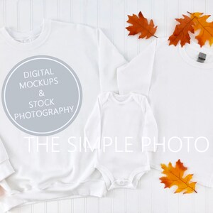 Peut inclure: Sweat-shirt blanc à manches longues, t-shirt blanc à manches longues et body blanc pour bébé sur un fond en bois blanc avec des feuilles d'automne. Le sweat-shirt a un cercle gris avec le texte "DIGITAL MOCKUPS & STOCK PHOTOGRAPHY THE SIMPLE PHOTO".