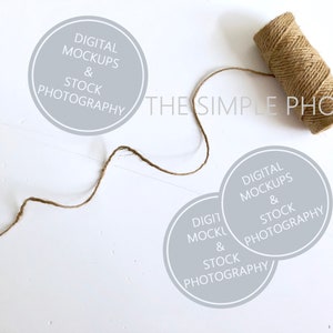 Könnte beinhalten: Zwei graue Kreise mit dem Text "DIGITAL MOCKUPS & STOCK PHOTOGRAPHY" auf weißem Hintergrund. Ein braunes Bindfadenband liegt auf der Oberfläche.