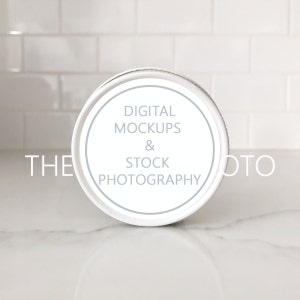 May include: A white, round container with a light blue rim and the text "DIGITAL MOCKUPS & STOCK PHOTOGRAPHY" in the center. The container sits on a white marble surface, with a white tile background.
