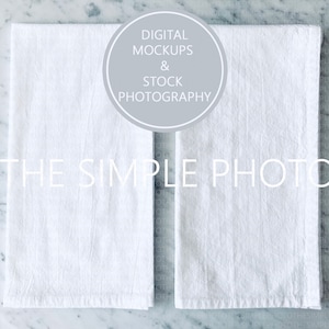 May include: Two white kitchen towels on a marble countertop. The towels are folded in half and have a slightly textured surface. The text "THE SIMPLE PHOTO" is printed in black on the towels.