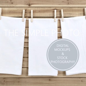 Puede incluir: Tres toallas de cocina blancas colgadas de una cuerda de ropa de madera con pinzas. Las toallas están en blanco y listas para ser personalizadas. El texto "THE SIMPLE PHOTO" es visible en el fondo.