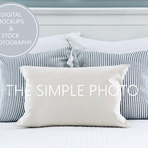 May include: A white bed with a white headboard and white bedding. There are three pillows on the bed, two with black and white stripes and one plain white pillow. The pillows are arranged in a staggered pattern.
