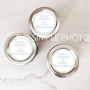 Op de afbeelding: Drie zilveren deksels van potten met witte etiketten waarop "DIGITAL MOCKUPS & STOCK PHOTOGRAPHY" staat.