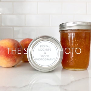 May include: A silver jar with a white label that reads "Digital Mockups & Stock Photography" sits on a white countertop next to two ripe peaches.