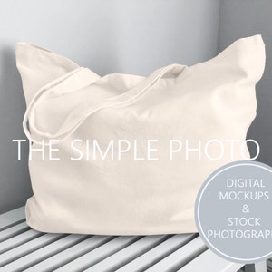 May include: A plain white canvas tote bag with a long handle. The bag is sitting on a white wooden bench. The text "THE SIMPLE PHOTO" is visible in the image. The text "DIGITAL MOCKUPS & STOCK PHOTOGRAPHY" is visible in a circle.