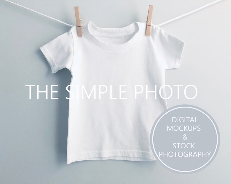 Puede incluir: Una camiseta blanca colgada de una cuerda para tender la ropa con pinzas de madera. La camiseta est&aacute; en blanco y lista para personalizar. El texto "THE SIMPLE PHOTO" est&aacute; impreso debajo de la camiseta. El texto "DIGITAL MOCKUPS & STOCK PHOTOGRAPHY" est&aacute; impreso en un c&iacute;rculo debajo del texto.