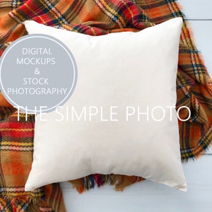 May include: A white pillow with a frayed edge sits on top of a plaid blanket with orange, brown, and black colors. The pillow is blank and ready for customization.