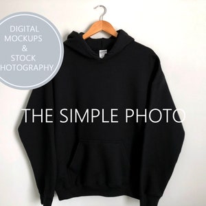 May include: Black hooded sweatshirt with a pouch pocket. The sweatshirt is hanging on a wooden hanger against a white background.