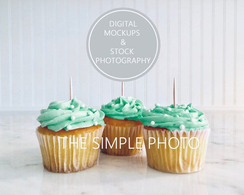 May include: Three green frosted cupcakes with white sprinkles on top, sitting on a white marble surface. A grey circle with the text "DIGITAL MOCKUPS & STOCK PHOTOGRAPHY" is in the background.