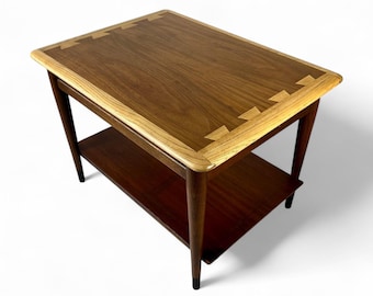 May include: A rectangular wooden side table featuring a dark brown walnut top with a lighter oak border and visible dovetail joinery at the corners. The table has four tapered legs and a lower shelf, all constructed from dark wood.