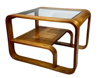 May include: A square side table featuring a light brown bentwood frame with a clear glass top and a lower shelf constructed from wood panels arranged in a geometric parquet pattern. The structure is open on all four sides.