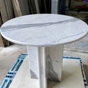 May include: A round marble table with a white and gray veined top. The table has a pedestal base with a cross-shaped design. The table is approximately 30 inches in diameter.