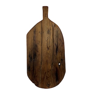 May include: A rustic, wooden cutting board with a handle. The board is made of dark brown wood with visible grain and knots. The irregular shape and natural finish give it a vintage, farmhouse aesthetic. Ideal for kitchen decor or food preparation.