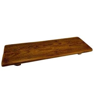 May include: A rectangular wooden serving tray with a rich brown finish. The tray has a natural wood grain pattern and is elevated slightly by small, round feet. The design is simple and rustic.