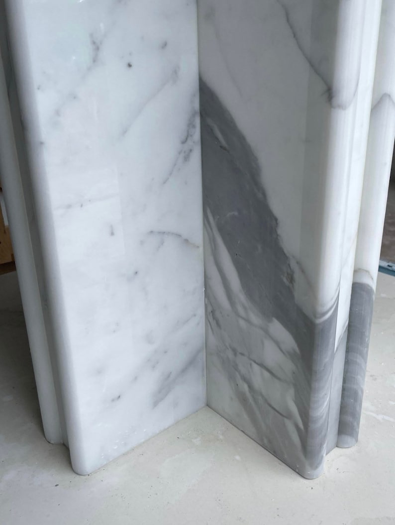 May include: Close-up of a section of a white marble structure with gray veining. The marble has a polished finish and is cut into a rectangular shape with rounded edges. The veining creates a natural pattern.