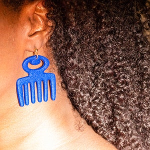 May include: A pair of blue comb-shaped earrings with a gold hook. The earrings are made of a smooth, glossy material.