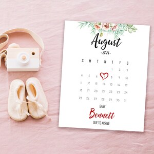 May include: A white calendar with the month of August 2024 highlighted. The 14th is marked with a red heart. The text "BABY Bennett DUE TO ARRIVE" is at the bottom of the calendar.