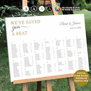 May include: A white wedding seating plan on an easel, featuring gold lettering. The chart displays guest names alphabetically, with the phrase "We've saved you a seat". The wedding date is June 11, 20XX.