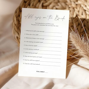 May include: A printable bridal shower game with the title "All eyes on the Bride". The game asks guests to guess details about the bride's outfit, such as the color of her outfit, the type of shoes she is wearing, and whether she is wearing earrings.
