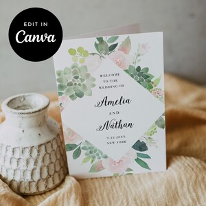 Puede incluir: Una invitación de boda con diseño floral y suculento en acuarela. La invitación dice "Bienvenida a la boda de Amelia y Nathan" con la fecha y el lugar. Un círculo negro con "Edit in Canva" está en la parte superior izquierda.