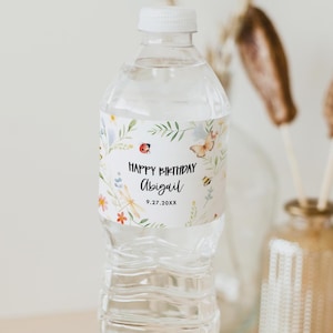 May include: Water bottle label with a floral design featuring butterflies, ladybugs, and dragonflies. The label says "Happy Birthday Abigail 9.27.20XX".