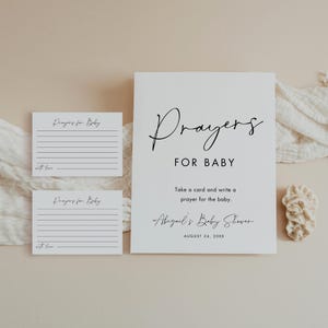 May include: A white sign with the words "Prayers FOR BABY" in elegant script, along with two smaller cards. The sign includes the text "Take a card and write a prayer for the baby" and "Abigail's Baby Shower".