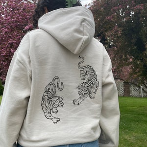 May include: A cream-coloured hoodie with a black and white tiger graphic on the back.