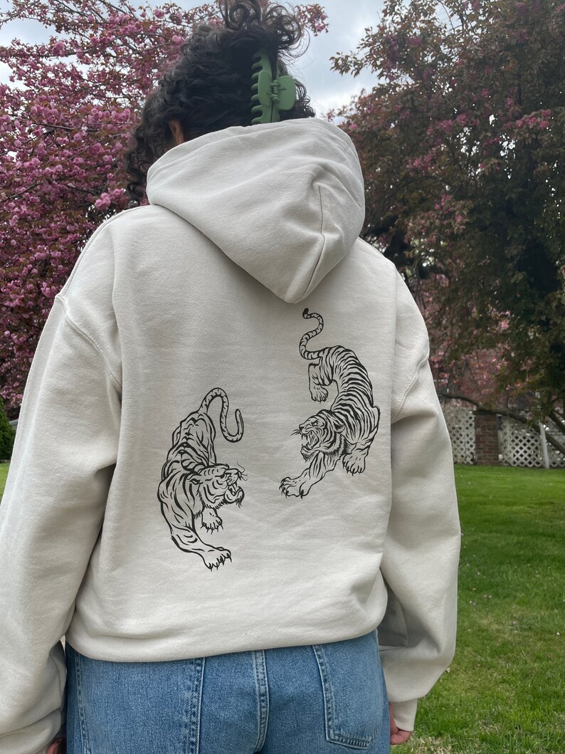 May include: A cream-coloured hoodie with a black and white tiger graphic on the back.