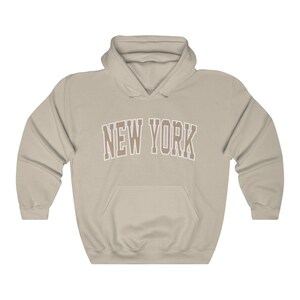 May include: A beige hooded sweatshirt with the text "NEW YORK" in brown letters with a white outline.
