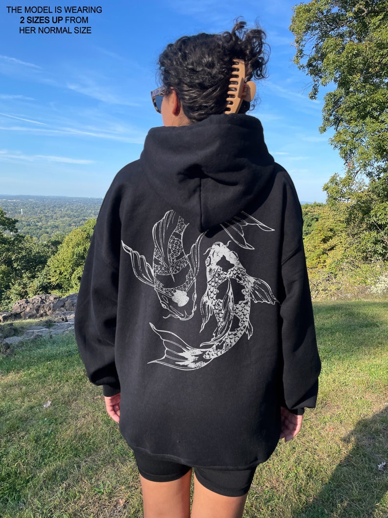 May include: Black oversized hoodie with a white graphic of two koi fish swimming. The hoodie has a drawstring hood.
