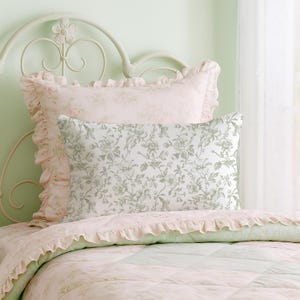 May include: A bed with a white metal headboard and floral bedding. The pillows have a ruffled edge and a floral pattern in shades of pink and green. The quilt has a patchwork design with a floral pattern.