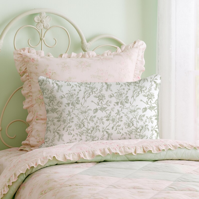 May include: A bed with a white metal headboard and floral bedding. The pillows have a ruffled edge and a floral pattern in shades of pink and green. The quilt has a patchwork design with a floral pattern.