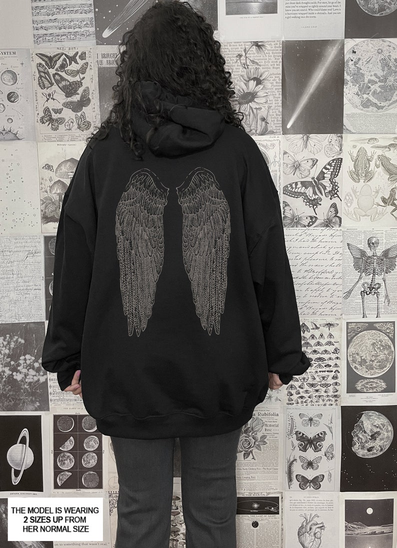 Pu&ograve; includere: Felpa con cappuccio nera oversize con una grafica di ali d'angelo argentate sul retro. Il modello indossa la felpa due taglie in pi&ugrave; rispetto alla sua taglia normale.
