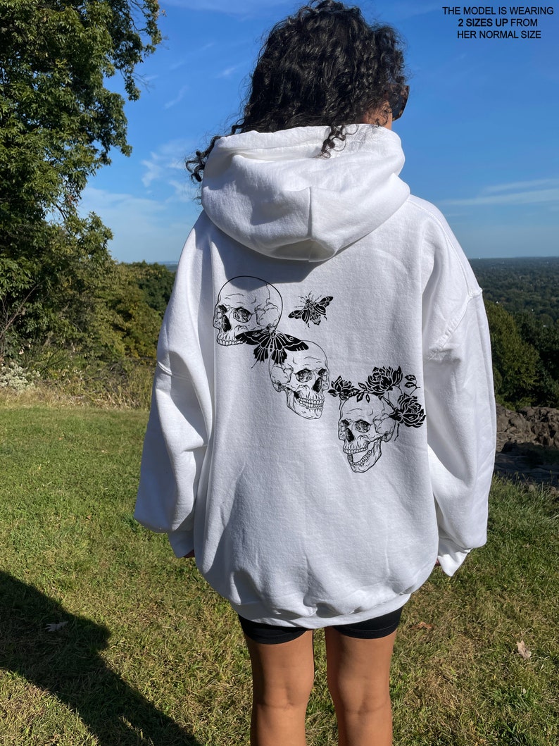 May include: White hooded sweatshirt with a black and white graphic print of three skulls with butterflies and flowers on the back.