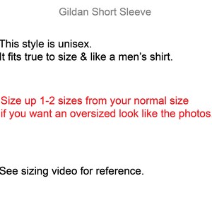 May include: Text on a white background explaining that this style of shirt is unisex and fits true to size. It also says to size up 1-2 sizes for an oversized look. The text also says to see the sizing video for reference.