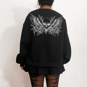 May include: Black sweatshirt with a white graphic print of a skull with wings and roses.