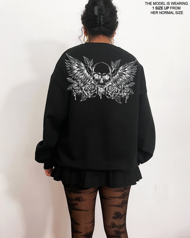 May include: Black sweatshirt with a white graphic print of a skull with wings and roses.