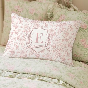 May include: A bed set with a floral pattern in pink and green. The focal point is a rectangular pillow with a pink floral design and a shield with the letter "E" and the name "EMILY MARIE".