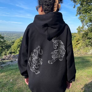 May include: Black oversized hoodie with a white tiger graphic on the back. The model is wearing the hoodie two sizes up from her normal size.