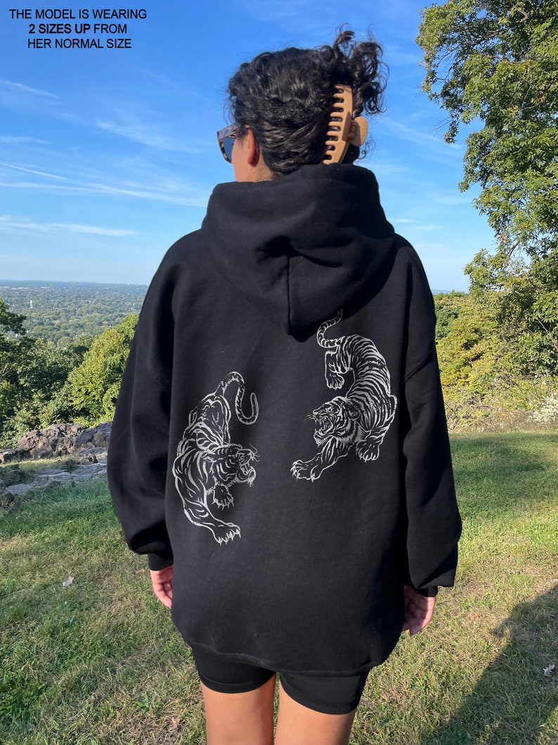 May include: Black oversized hoodie with a white tiger graphic on the back. The model is wearing the hoodie two sizes up from her normal size.
