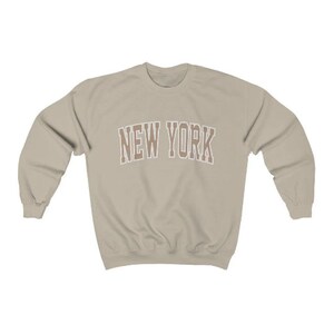 May include: A beige sweatshirt with the text "NEW YORK" in brown letters with a white outline.
