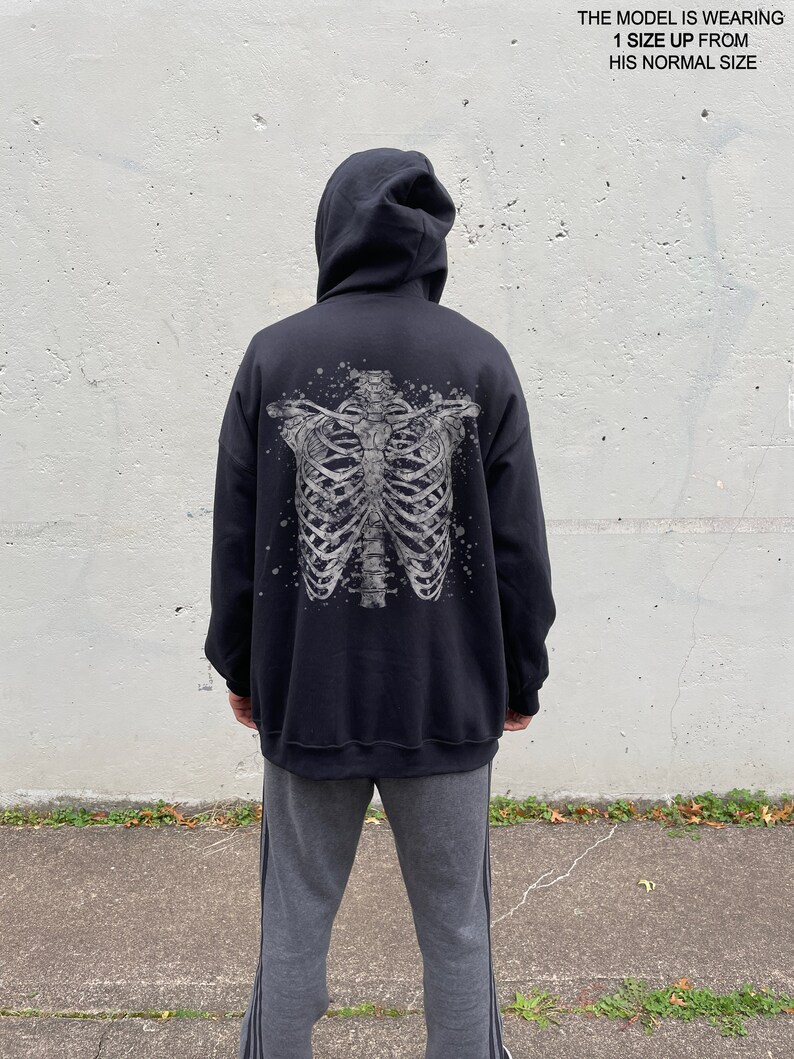 May include: Black hooded sweatshirt with a white skeleton print on the back. The model is wearing the sweatshirt one size up from their normal size.
