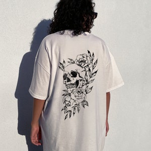 May include: White oversized t-shirt with a black skull and floral design on the back. The model is wearing the shirt two sizes up from her normal size.