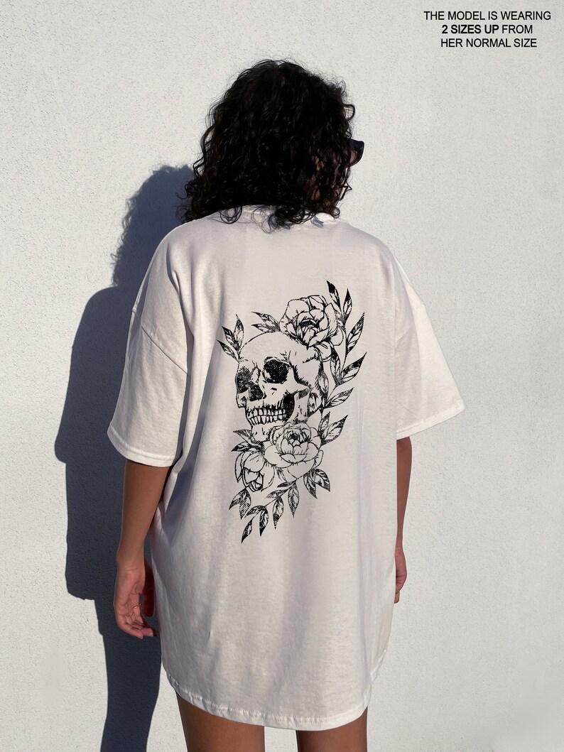 May include: White oversized t-shirt with a black skull and floral design on the back. The model is wearing the shirt two sizes up from her normal size.