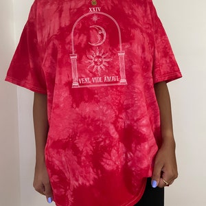 May include: Red tie-dye t-shirt with a white graphic of a sun, moon, and archway with the text "XXIV" and "VENI. VIDI. AMAVI."