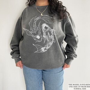 May include: A grey sweatshirt with a white graphic of two koi fish swimming in a circle. The model is wearing one size up from her usual size.