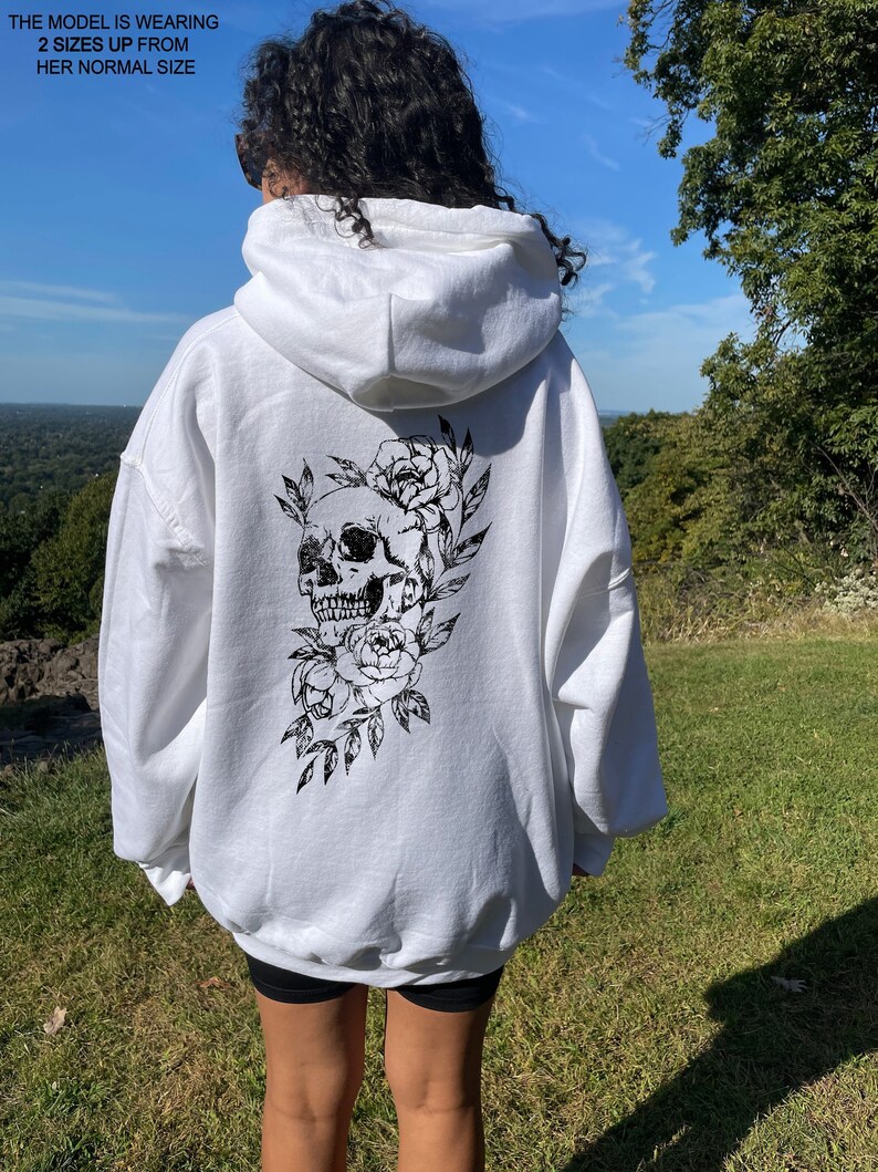 Puede incluir: Sudadera blanca de gran tama&ntilde;o con un dise&ntilde;o de calavera negra y flores en la espalda.