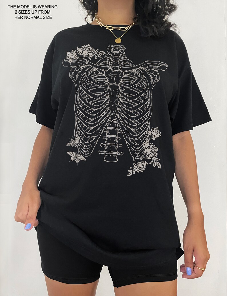 K&ouml;nnte beinhalten: Schwarzes Oversize-T-Shirt mit einem wei&szlig;en Aufdruck eines Brustkorbs mit Blumen und Schmetterlingen.