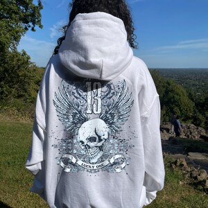 May include: White hooded sweatshirt with a blue and white skull graphic on the back. The graphic features wings, a skull, and the text "Lucky One".