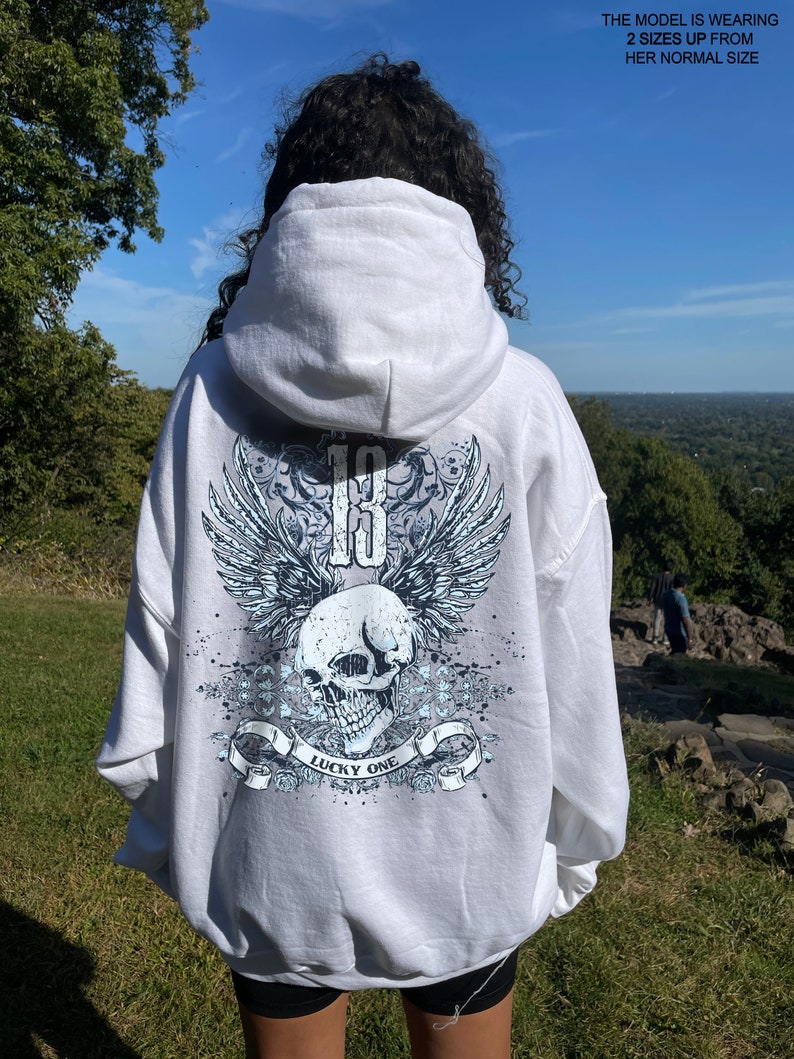 May include: White hooded sweatshirt with a blue and white skull graphic on the back. The graphic features wings, a skull, and the text "Lucky One".